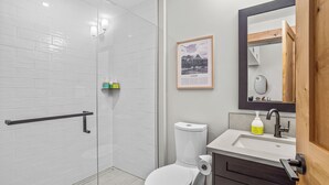 Un bagno moderno con cabina doccia in vetro, un WC, un lavandino con specchio e un quadro appeso alla parete.