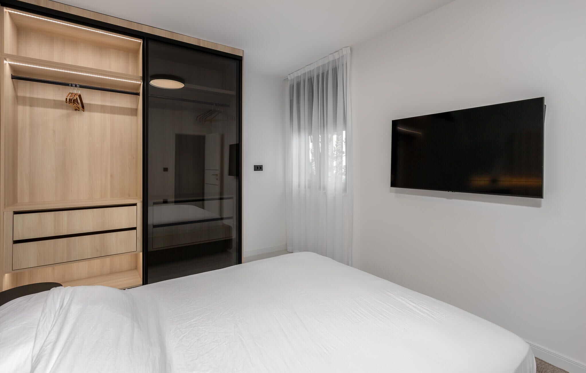 A modern hotel room with a bed, a wardrobe, a mirror, and a TV.