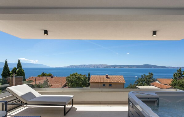 Een balkon met een jacuzzi, ligstoelen en uitzicht op de zee en verre bergen.