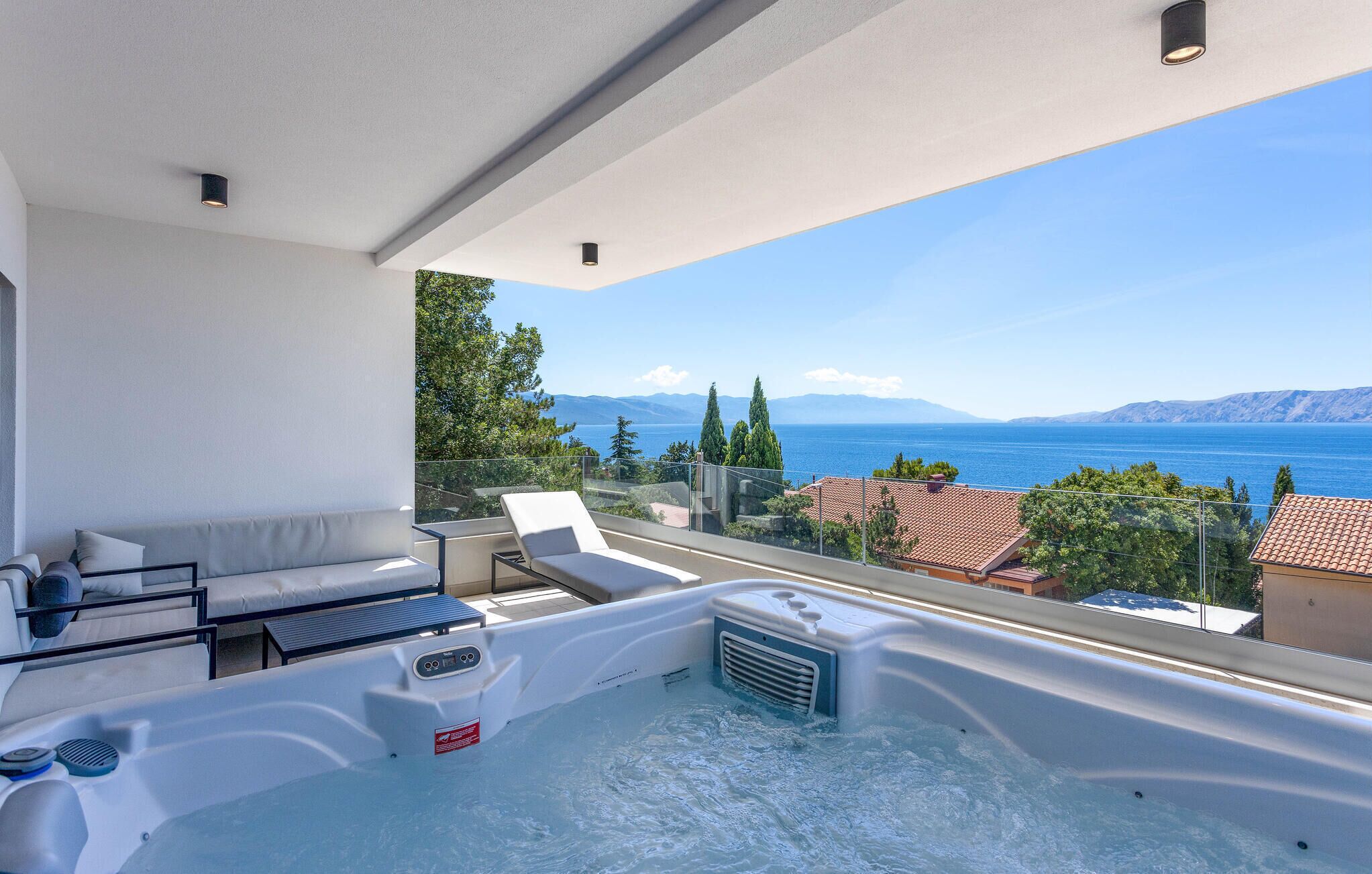 A balcony with a hot tub, a sofa, and a view of the sea and mountains.
