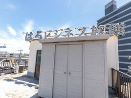 Un edificio con un cartel grande de caracteres japoneses, una puerta metálica cerrada y una barandilla de metal.