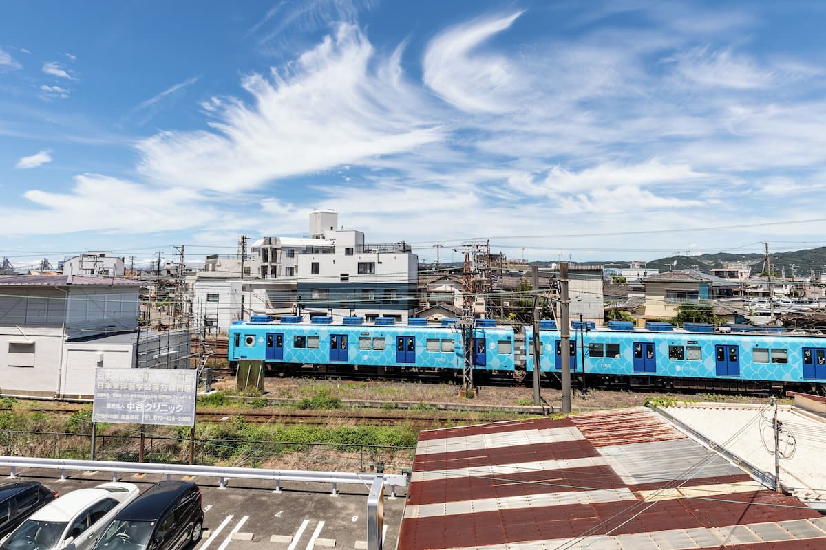 Un train bleu circule sur des voies ferrées, avec des bâtiments en arrière-plan.