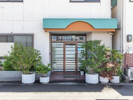 Un edificio con un toldo verde y un letrero en japonés. Hay plantas en macetas frente a la entrada.