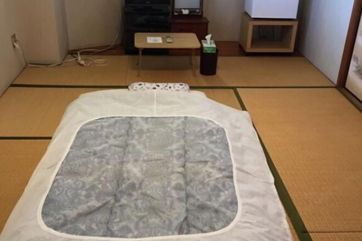 Een kamer met tatami matten, een futonbed, een tafeltje en een prullenbak.