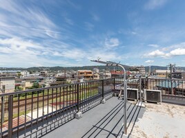 Una terraza con barandilla de metal que ofrece vistas a un paisaje urbano, con edificios y una vía de tren.