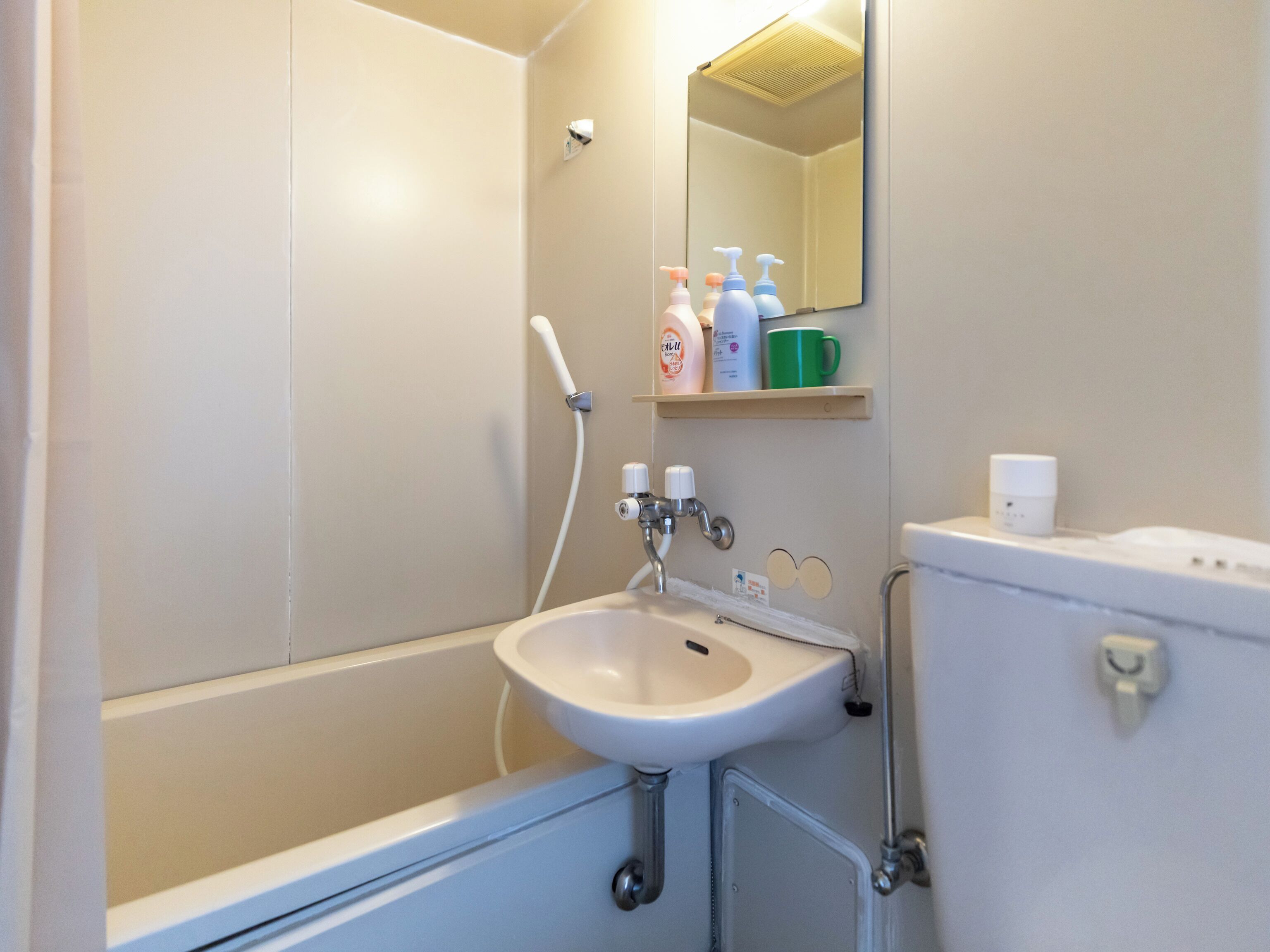 A bathroom with a bathtub, sink, and toilet. There are toiletries on a shelf above the sink.