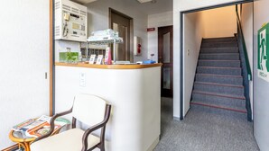 A hotel lobby with a reception desk, a staircase, and a seating area with a chair and table. - Tabist Hara Business Ryokan (Wakayama)