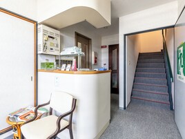 Un hall de hotel con una recepción, una escalera y un área de descanso con una silla y una mesa.