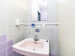 Une salle de bain avec un lavabo blanc, un miroir et une étagère contenant des articles de toilette.
