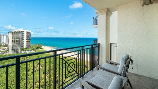 A balcony with a view of the ocean and beach, featuring a table and chairs. - Palm Beach Singer Island Resort & Spa Luxury Suites 2/2 Ocean View (Riviera Beach)