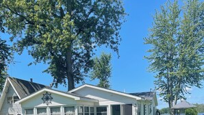 Une maison mobile blanche dotée d’un patio couvert, d’une cour clôturée et d’un grand arbre en arrière-plan.