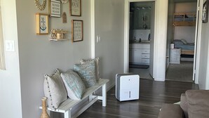 Un salon avec un canapé blanc, un canapé marron et une petite table blanche. Des tableaux encadrés ornent le mur, et un vase en bois est posé sur le sol.