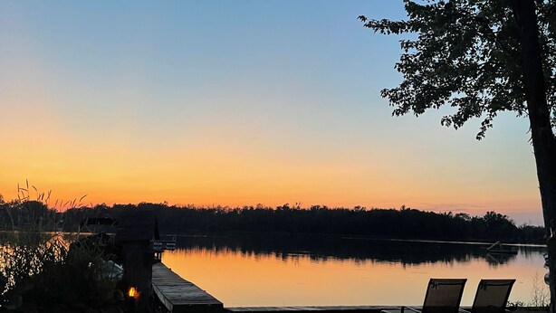 Une vue sur le lac au crépuscule, avec une jetée en bois et des chaises longues.