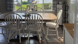 Un coin repas avec vue sur un lac, des chaises blanches, une table en bois et un ventilateur de plafond.