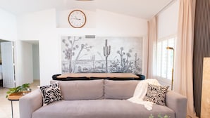 A modern living room with a grey sofa, a coffee table, and a large cactus painting on the wall. - Welcome to Casa Jubilant Cacti by HomeSlice Stays (Phoenix)
