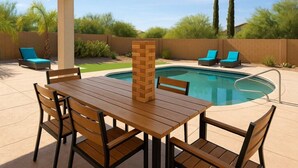 A poolside area with a wooden table and chairs, a brick pillar, and two lounge chairs. - Welcome to Casa Jubilant Cacti by HomeSlice Stays (Phoenix)