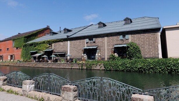 Ein Gebäude am Flussufer mit Backsteinwänden, grünen Markisen und einer Terrasse.