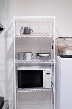 Uma cozinha com um micro-ondas branco numa prateleira, uma cafeteira e um saleiro.