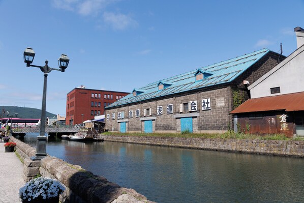 A waterfront building with a blue roof and stone walls, a canal in front, and a bridge in the background. - aquamarine (Otaru)