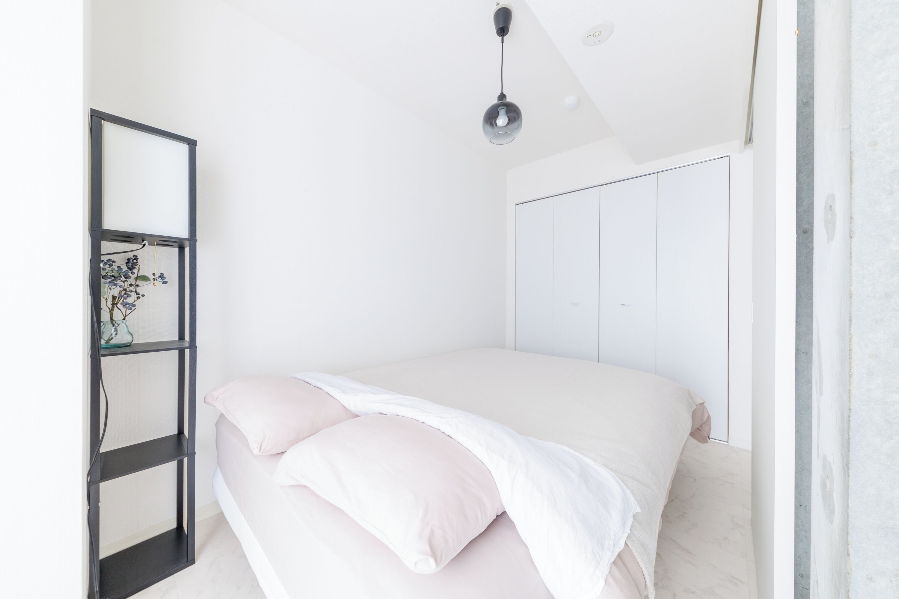A bedroom with a bed, a bedside table, a mirror, and a hanging light fixture.