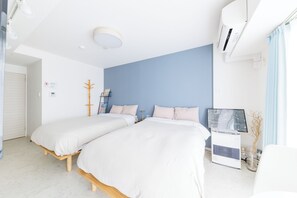 Quarto de hotel com duas camas de solteiro, televisão de tela plana, ar condicionado e uma mesinha com um vaso.