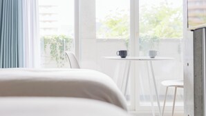Ein Hotelzimmer mit Bett, einem kleinen Tisch mit zwei Tassen und Blick auf Grünflächen.