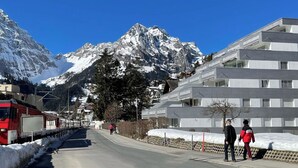 Um edifício moderno com telhado plano e várias janelas, situado perto de uma montanha coberta de neve.