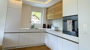 A modern kitchen with white cabinetry, a built-in oven, and a window with a view of a house. - Sunnmatt West Wohnung 933 Appartement/Fewo 5-Bettwohnung by Interhome (Engelberg)
