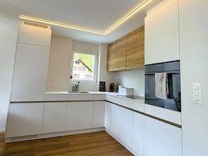 A modern kitchen with white cabinetry, a built-in oven, and a window with a view of a house. - Sunnmatt West Wohnung 933 Appartement/Fewo 5-Bettwohnung by Interhome (Engelberg)