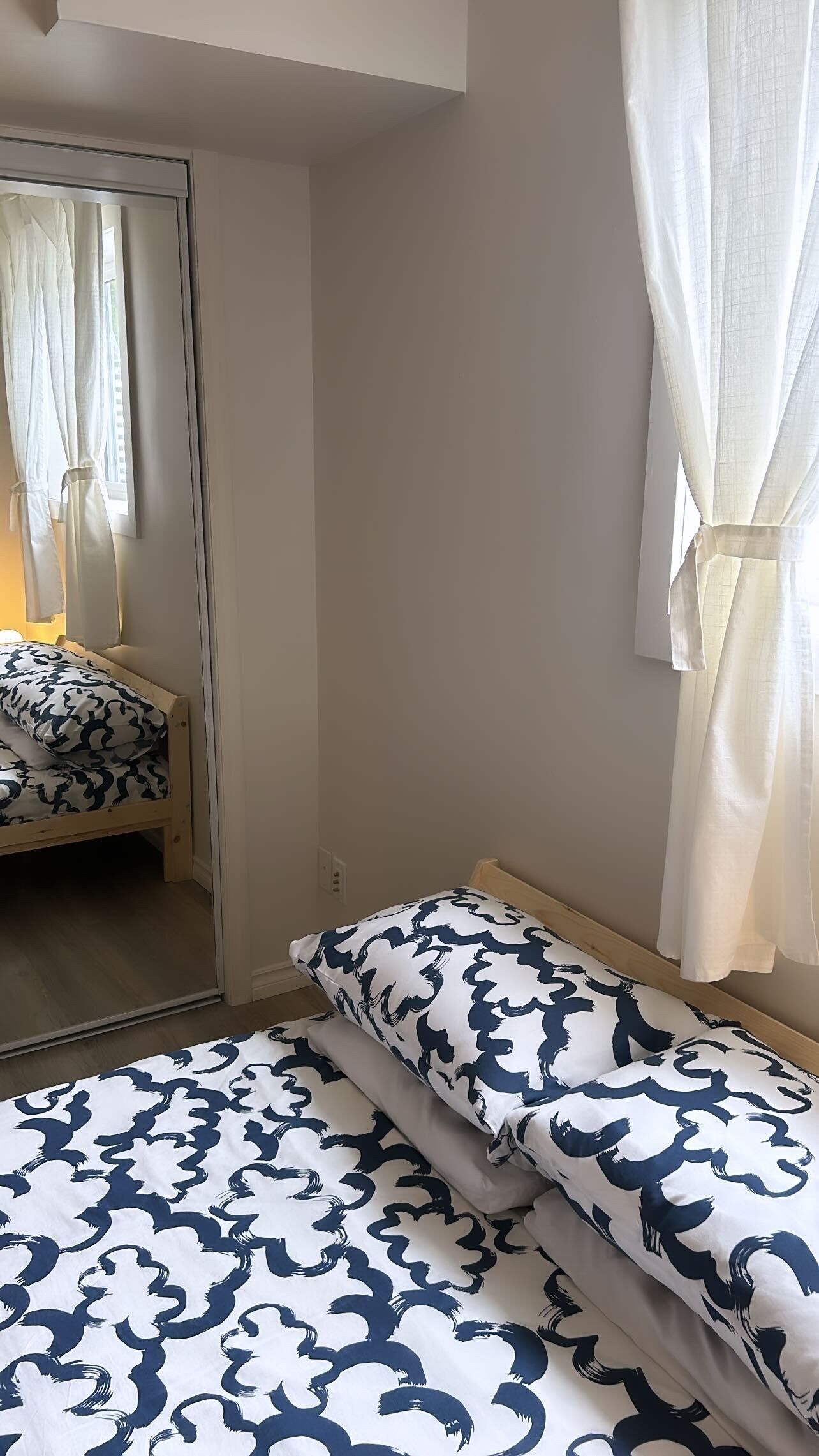 A bedroom with a bed, a mirror, and a window with curtains.