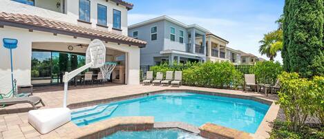 A swimming pool with a hot tub, lounge chairs, and a basketball hoop.