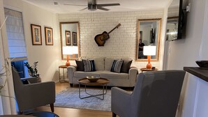 Un salon comprenant un canapé, deux fauteuils, une table basse, une guitare accrochée au mur et deux lampes.