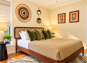 Una camera da letto con un letto, cuscini, un comodino con una lampada, un elemento decorativo a parete e opere d'arte incorniciate.