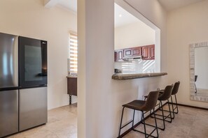Una cocina moderna con electrodomésticos de acero inoxidable, una zona de bar con taburetes y un espejo grande.