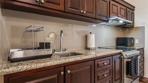 A kitchen with dark wood cabinets, a granite countertop, a stainless steel range hood, a built-in oven, and a microwave. - Tormenta 202 3BR Second Floor San Jose del Cabo (San José del Cabo)