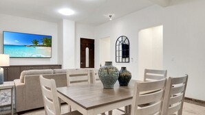 A dining area with a wooden table and chairs, two decorative vases, a television displaying a beach scene, and a door with a window. - Tormenta 101 3BR Ground Floor San Jose del Cabo (San José del Cabo)