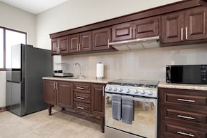 A kitchen with dark wooden cabinets, a stainless steel refrigerator, a gas stove, and a microwave. - Tormenta 101 3BR Ground Floor San Jose del Cabo (San José del Cabo)