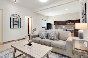 A living room with a sofa, a coffee table, a lamp, and a kitchen in the background. - Tormenta 101 3BR Ground Floor San Jose del Cabo (San José del Cabo)