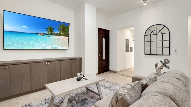 A living room with a large TV, a sofa, a coffee table, and a door leading to another room. - Tormenta 101 3BR Ground Floor San Jose del Cabo (San José del Cabo)