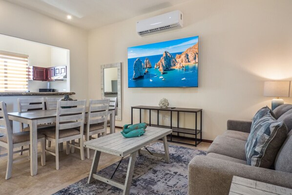 A living room with a dining area, a mounted TV, and a small table with a vase.
