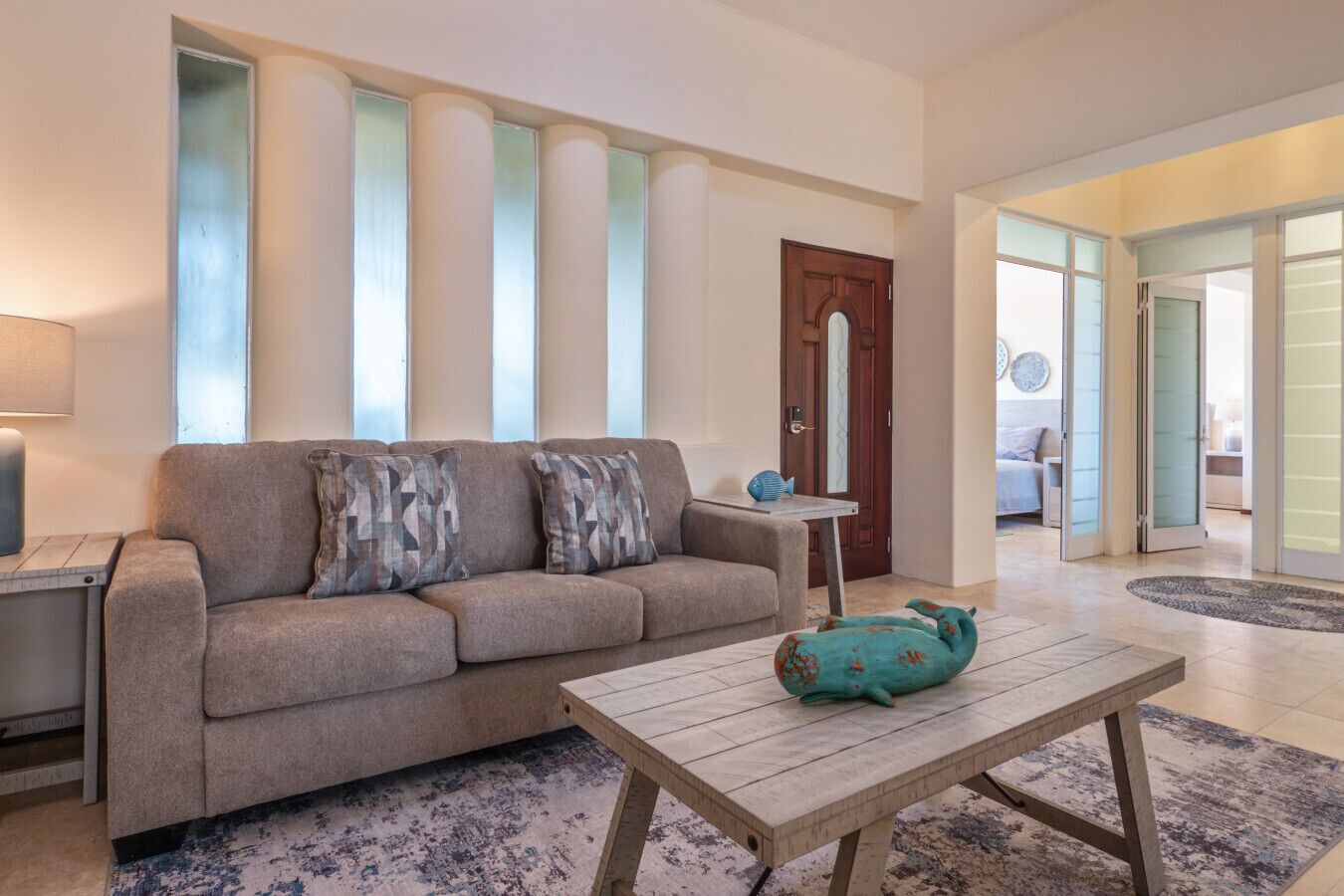 A living room with a sofa, a coffee table, a lamp, and a door.