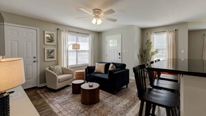 Un salon avec un canapé bleu foncé, un fauteuil beige, une table basse et un coin repas comprenant une table et des chaises noires.