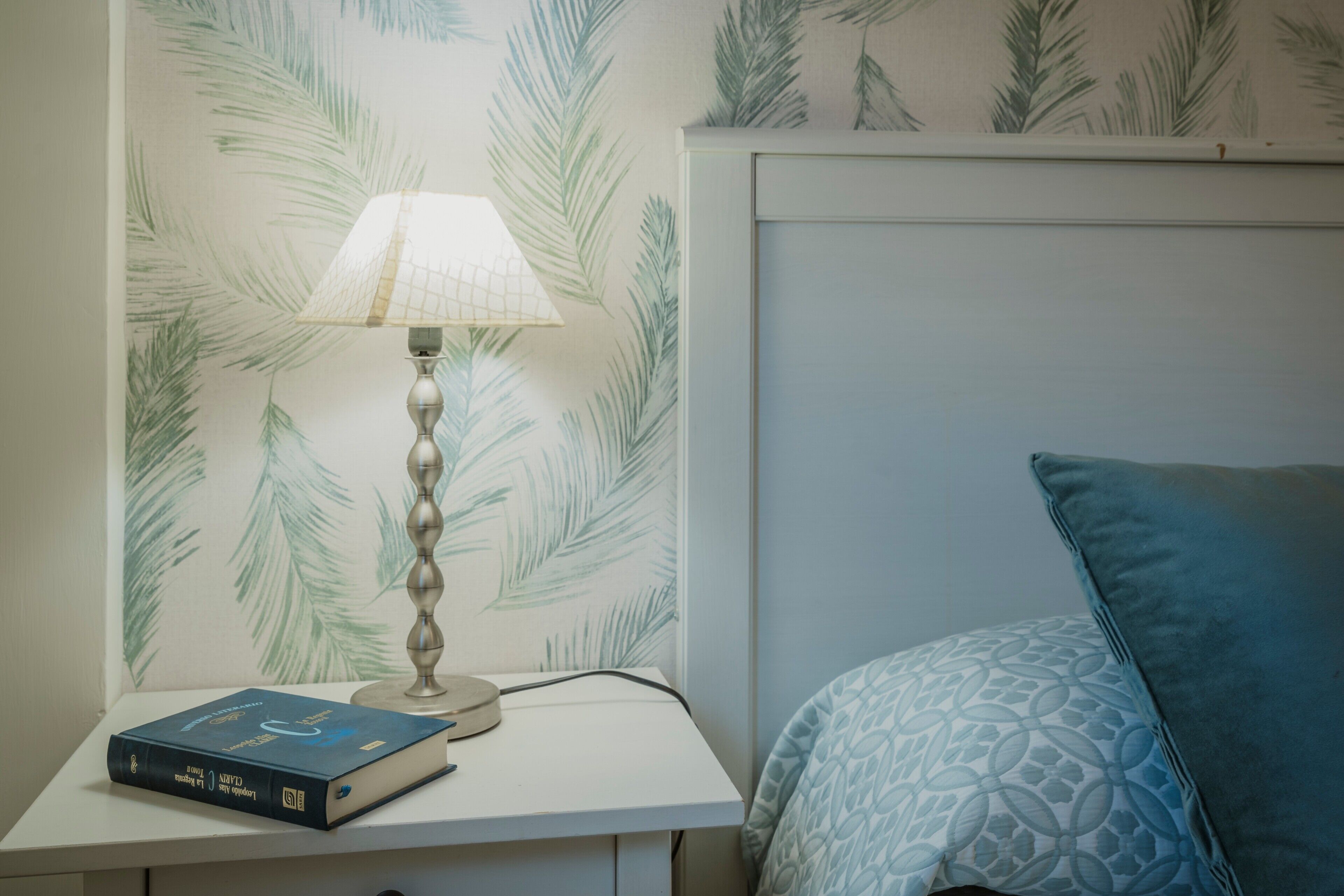 A bedside table with a lamp, a book, and a patterned pillow.