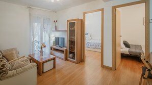 A modern living room with a sofa, TV, wooden cabinet, and a bed in the adjacent room.