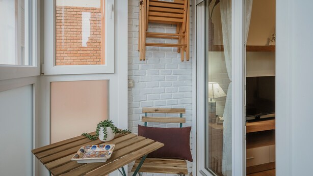 A small balcony with a wooden table, a chair, a potted plant, and a brick wall.