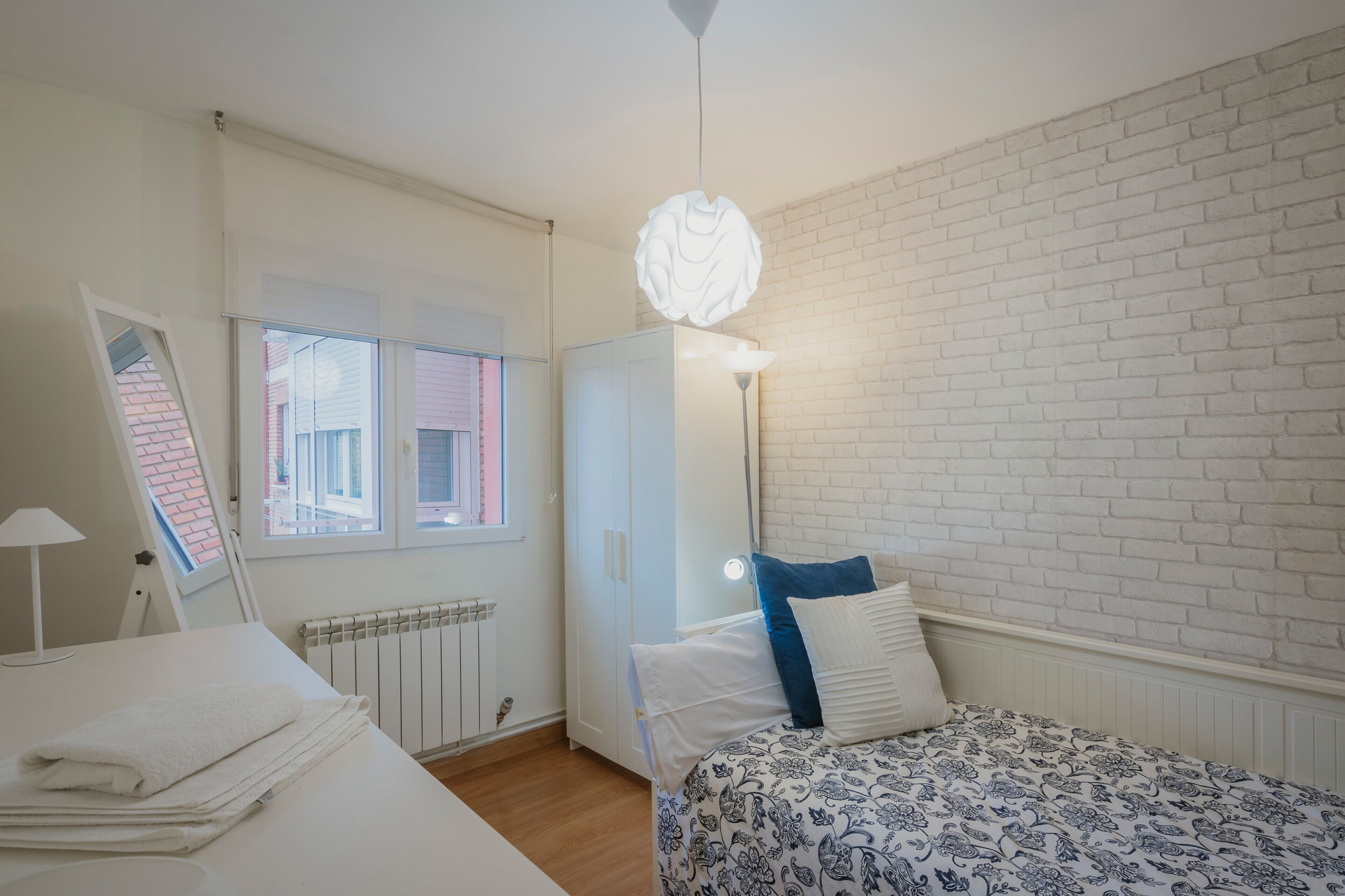 A bedroom with a bed, a radiator, a window, a wardrobe, and a hanging light fixture.