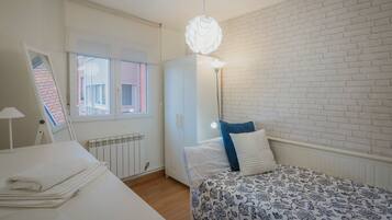 A bedroom with a bed, a radiator, a window, a wardrobe, and a hanging light fixture.