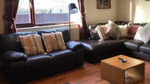 A living room with a dark leather sofa, a wooden coffee table, and a large window with curtains.