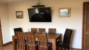 A dining room with a wooden table and chairs, a flat-screen TV mounted on the wall, and framed pictures on the walls.