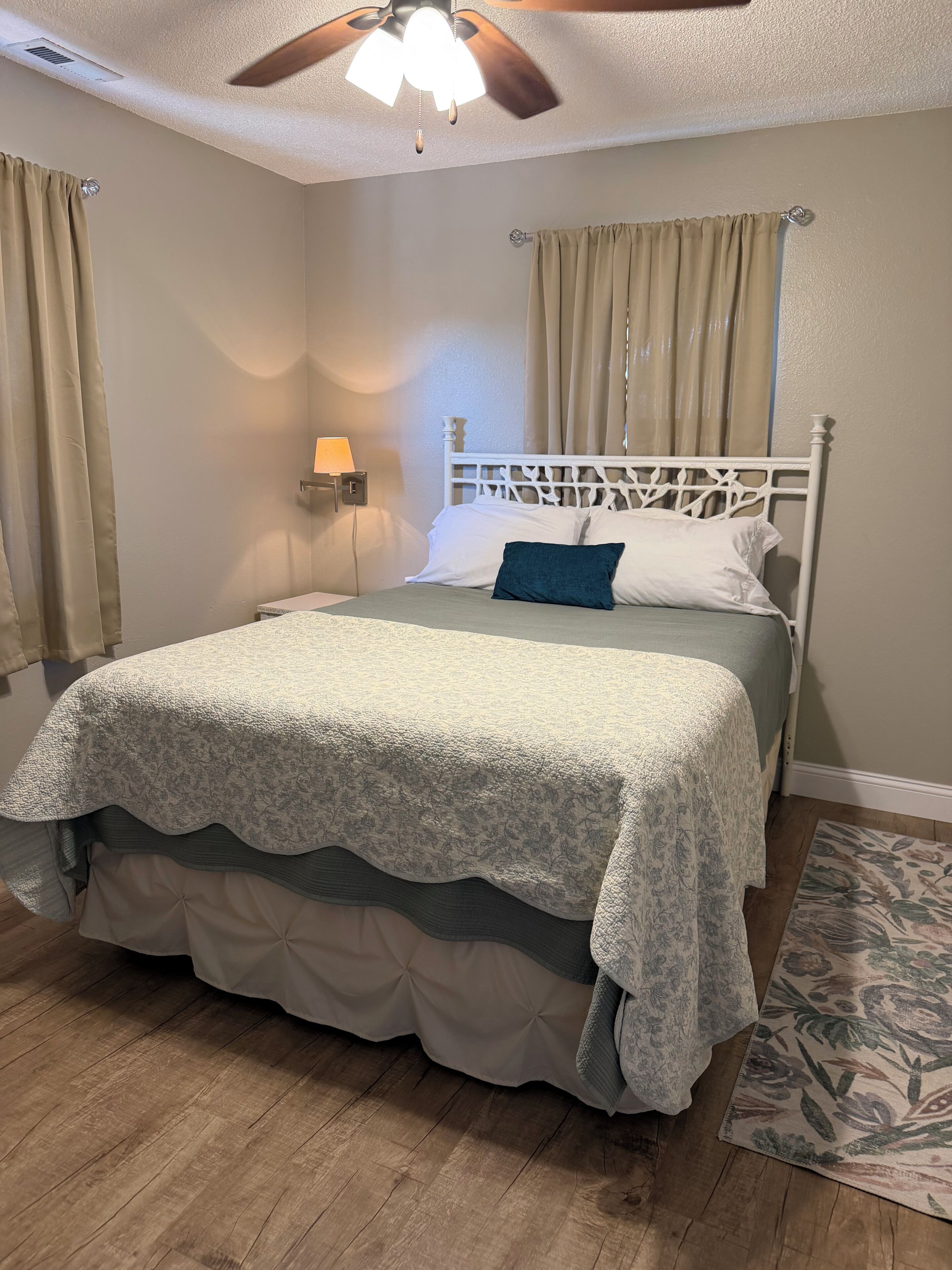 Un dormitorio con cama, ventilador de techo, mesita de noche y lámpara de pared.